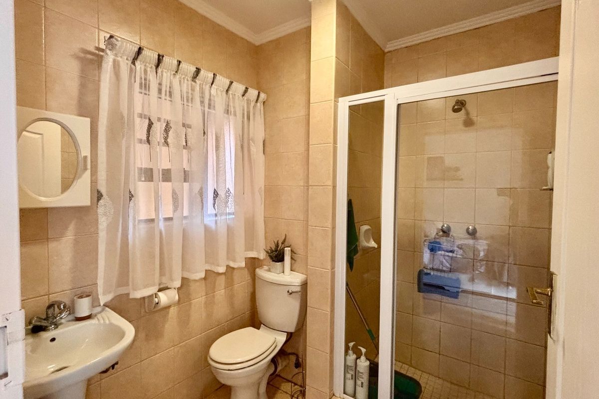 A functional bathroom featuring a pedestal sink, toilet, and a glass-enclosed shower with neutral wall and floor tiling.
