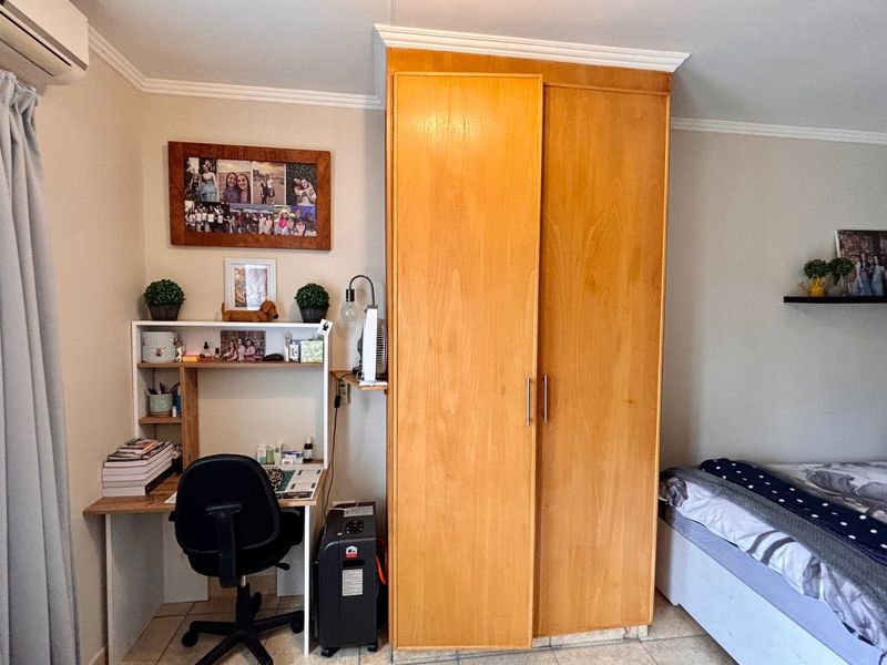 A bedroom featuring a large built-in wooden wardrobe, tiled flooring, crown molding, and a wall-mounted air conditioning unit.