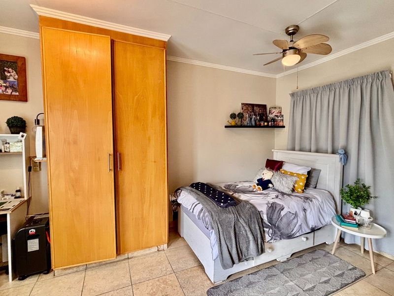 A bedroom featuring tiled flooring, a built-in wooden wardrobe, and a ceiling fan, offering a functional and comfortable living space.