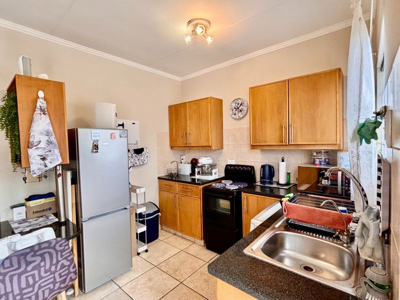 A functional kitchen featuring wooden cabinetry, granite countertops, a stainless steel sink, and a freestanding stove with tiled flooring.