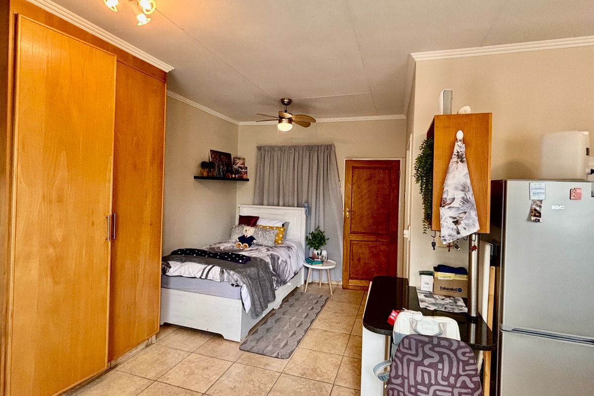 Open-plan studio apartment featuring tiled flooring, built-in wooden cupboards, a ceiling fan, and a compact kitchenette area with granite countertops.