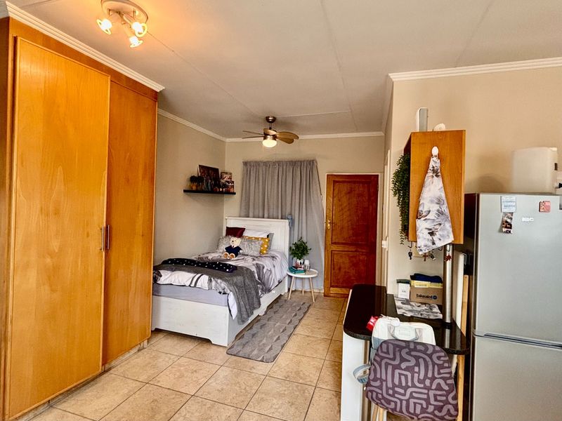 Open-plan studio apartment featuring tiled flooring, built-in wooden cupboards, a ceiling fan, and a compact kitchenette area with granite countertops.