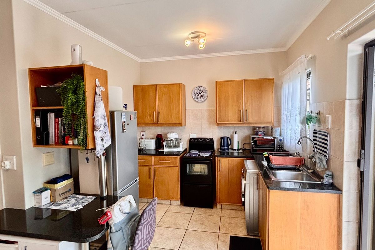 A functional kitchen featuring wooden cabinetry, granite countertops, a stainless steel sink, and tiled flooring, offering a practical layout for daily meal preparation.