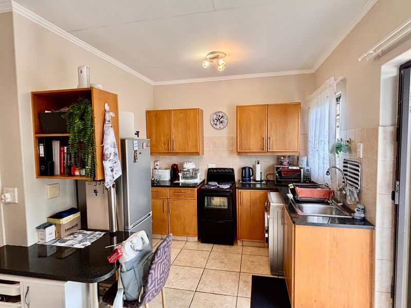 A functional kitchen featuring wooden cabinetry, granite countertops, a stainless steel sink, and tiled flooring, offering a practical layout for daily meal preparation.