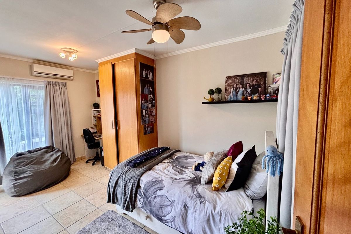 A well-maintained bedroom featuring tiled flooring, a ceiling fan, built-in wardrobe, and a split-system air conditioner with access to an outdoor area.