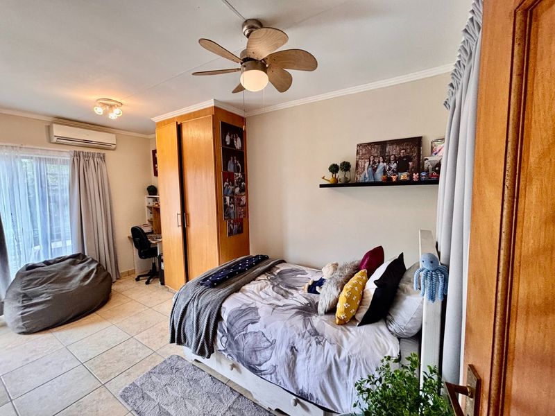 A well-maintained bedroom featuring tiled flooring, a ceiling fan, built-in wardrobe, and a split-system air conditioner with access to an outdoor area.