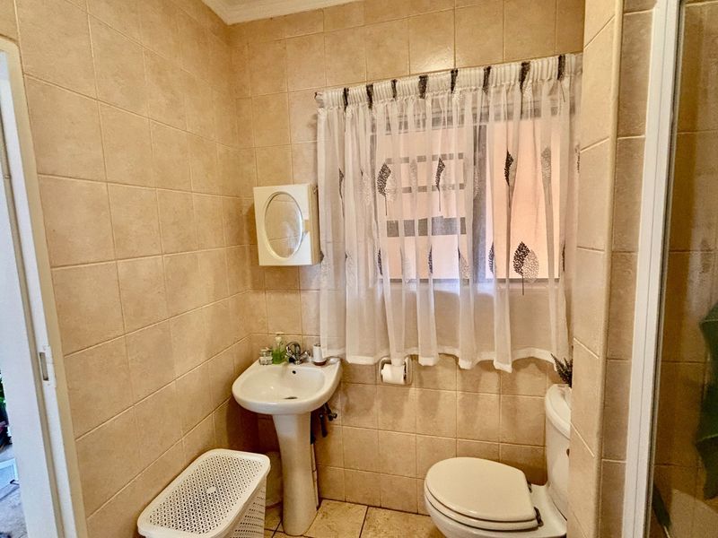 A functional bathroom featuring tiled walls and flooring, a pedestal basin, and a toilet, with natural light provided by a window.
