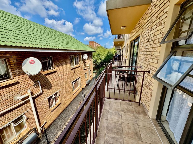 A functional balcony with tiled flooring and metal railings, overlooking the adjacent apartment building and surrounding greenery.