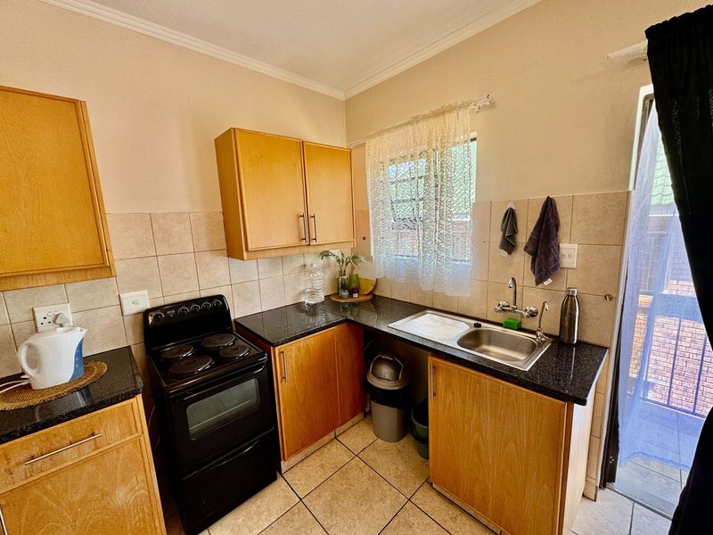 A functional kitchen featuring wood-finish cabinetry, granite countertops, a stainless steel sink, and a freestanding electric stove with tiled backsplash and flooring.