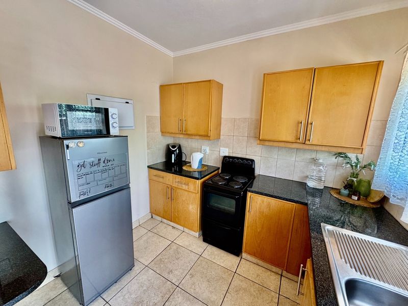 A functional kitchen featuring wooden cabinetry, granite countertops, tiled backsplash, and ceramic floor tiles, providing a practical workspace for daily cooking.