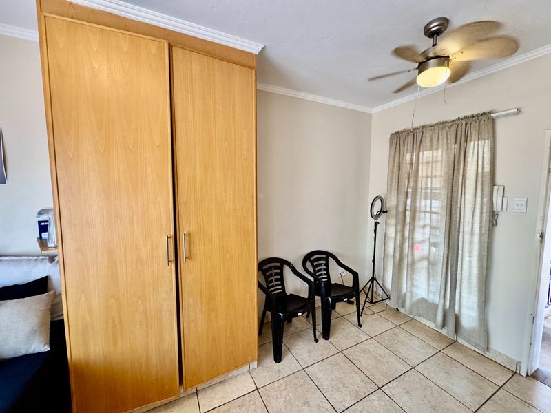 A bedroom featuring a built-in wooden wardrobe, tiled flooring, and a ceiling fan, offering a functional space with neutral finishes.