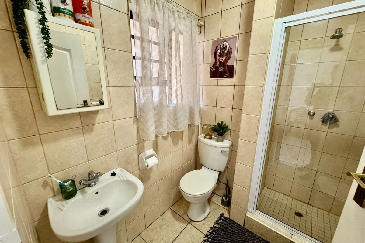 A functional bathroom featuring a pedestal basin, a shower enclosure with a fixed shower head, and a standard toilet, finished with neutral wall tiles.