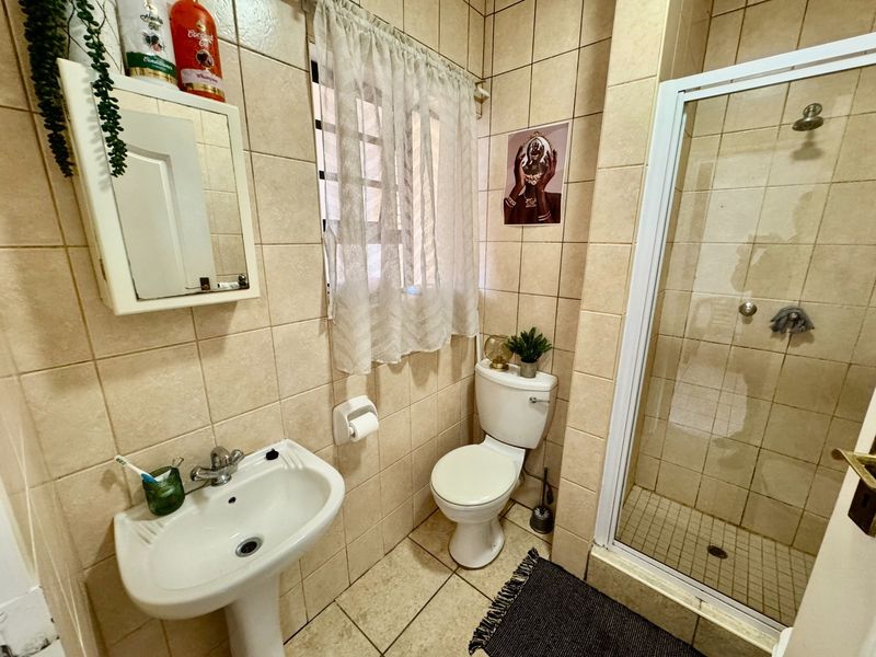 A functional bathroom featuring a pedestal basin, a shower enclosure with a fixed shower head, and a standard toilet, finished with neutral wall tiles.