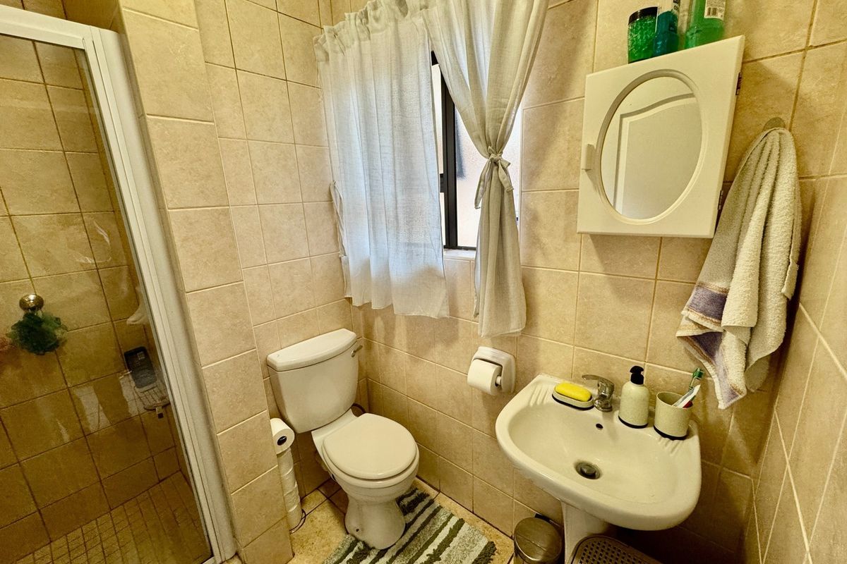 Compact bathroom featuring a shower enclosure, pedestal basin, and toilet with neutral wall tiling.