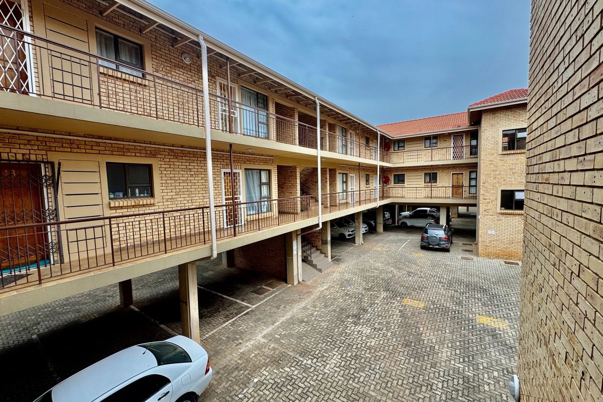 Exterior view of a multi-story apartment complex featuring face-brick facade, covered walkways, and ground-level paved parking area.