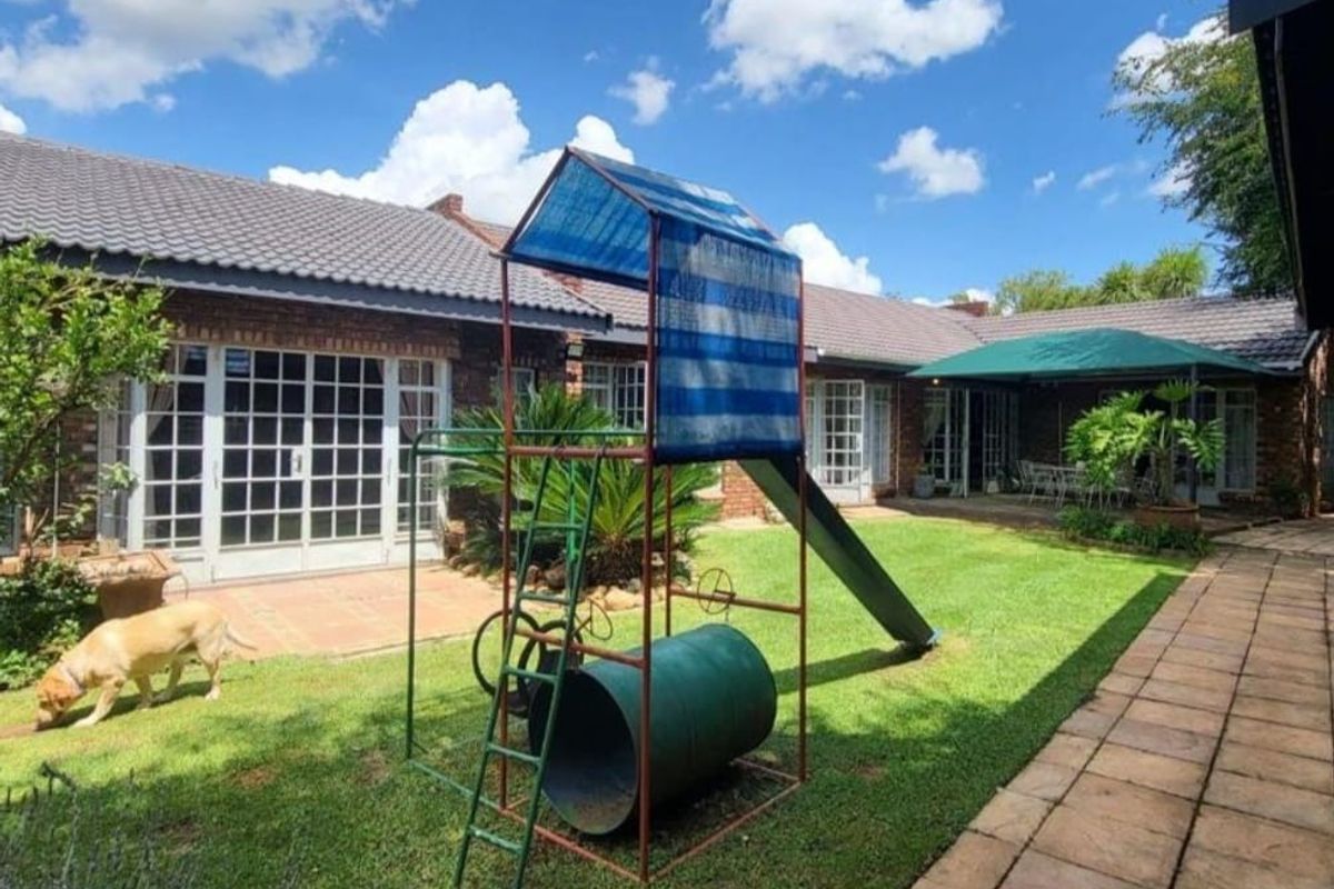 A spacious rear garden featuring a well-maintained lawn, paved pathways, and direct access to the home through multiple sets of french doors.
