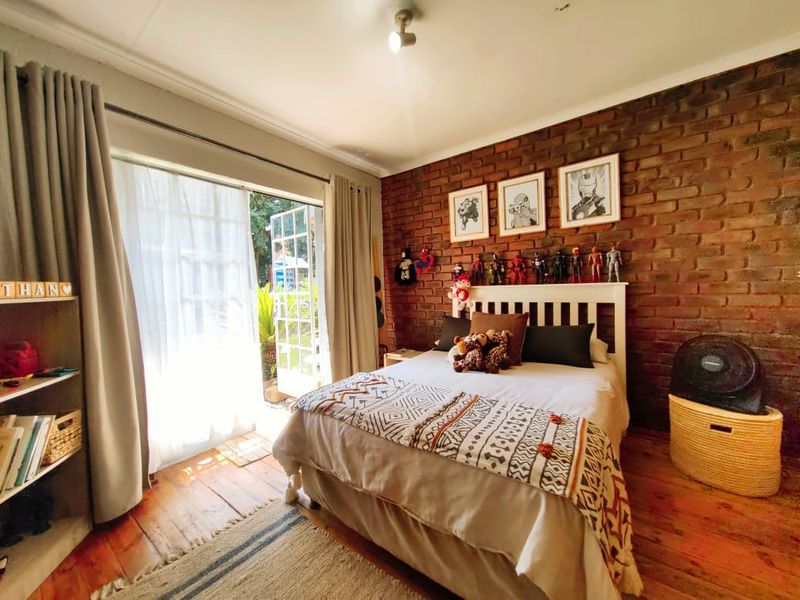 A bedroom featuring an exposed brick feature wall, timber flooring, and direct access to the outdoors through glass-paned french doors.