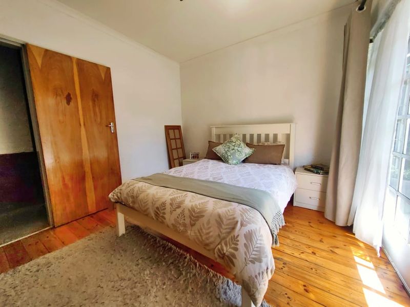 A bedroom featuring polished hardwood flooring, a wooden door, and a glass sliding door providing natural light.