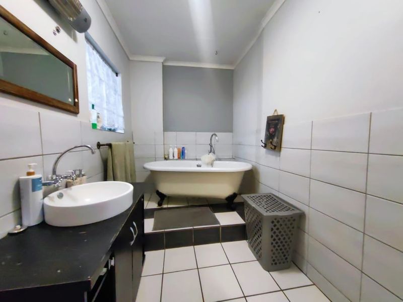 A bathroom featuring a classic freestanding bathtub, a modern vessel sink set on a vanity cabinet, and tiled wall and floor finishes.