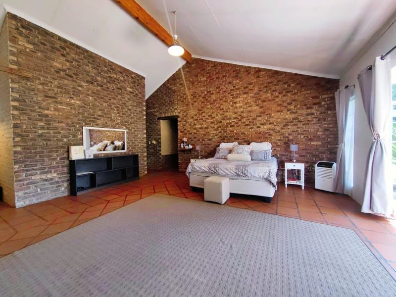 Spacious bedroom featuring high vaulted ceilings with exposed timber beams and distinctive exposed brick walls, complemented by traditional terracotta floor tiles.