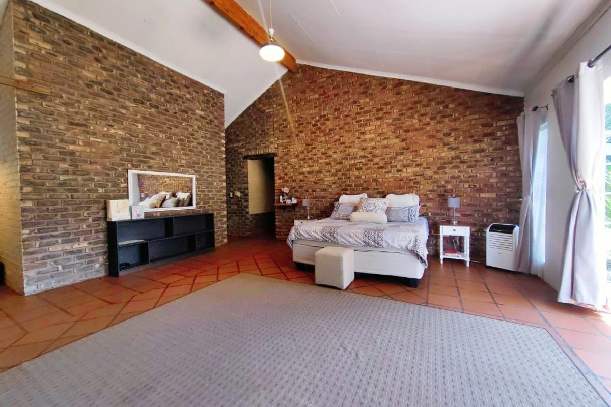 Spacious bedroom featuring high vaulted ceilings with exposed timber beams and distinctive exposed brick walls, complemented by traditional terracotta floor tiles.