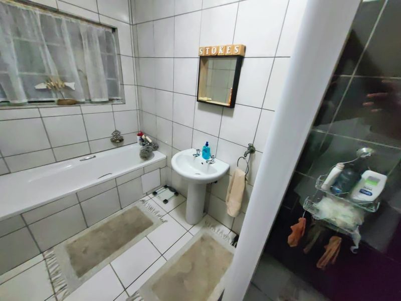 A functional bathroom featuring a pedestal basin, bathtub, and tiled finishes throughout, providing a standard layout for daily use.