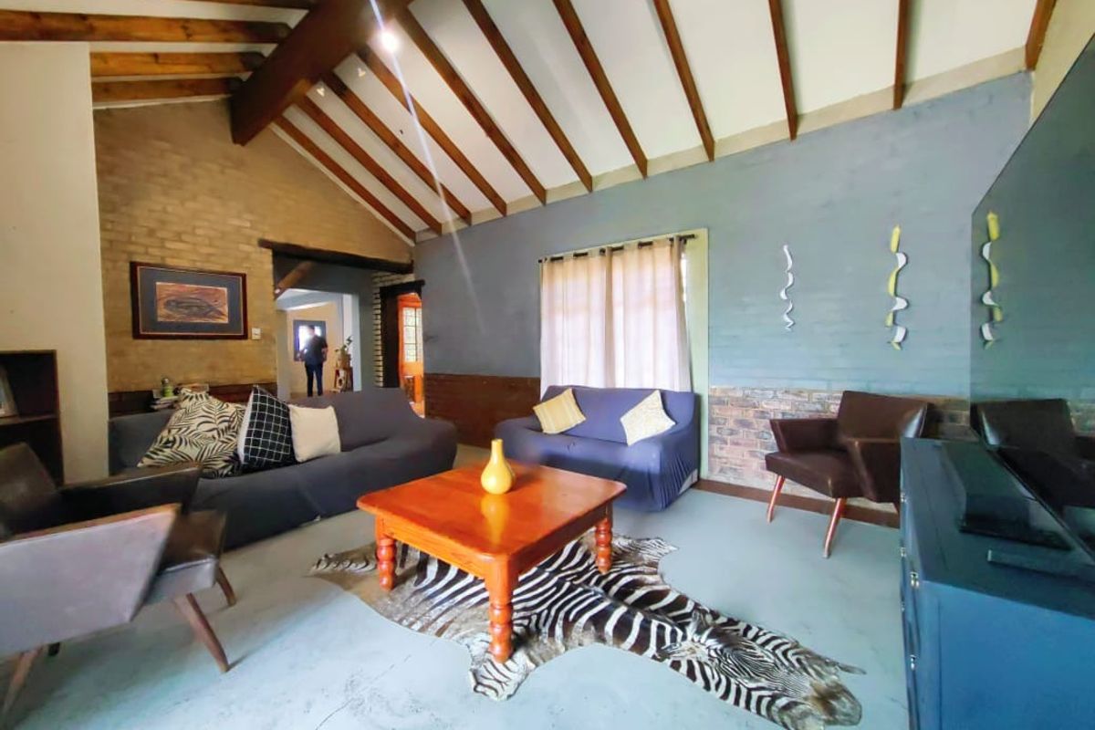 Spacious living room featuring a vaulted ceiling with exposed timber beams, concrete flooring, and a combination of exposed and painted brick walls.