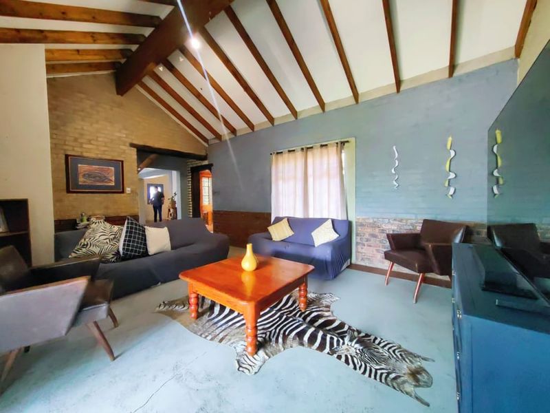 Spacious living room featuring a vaulted ceiling with exposed timber beams, concrete flooring, and a combination of exposed and painted brick walls.