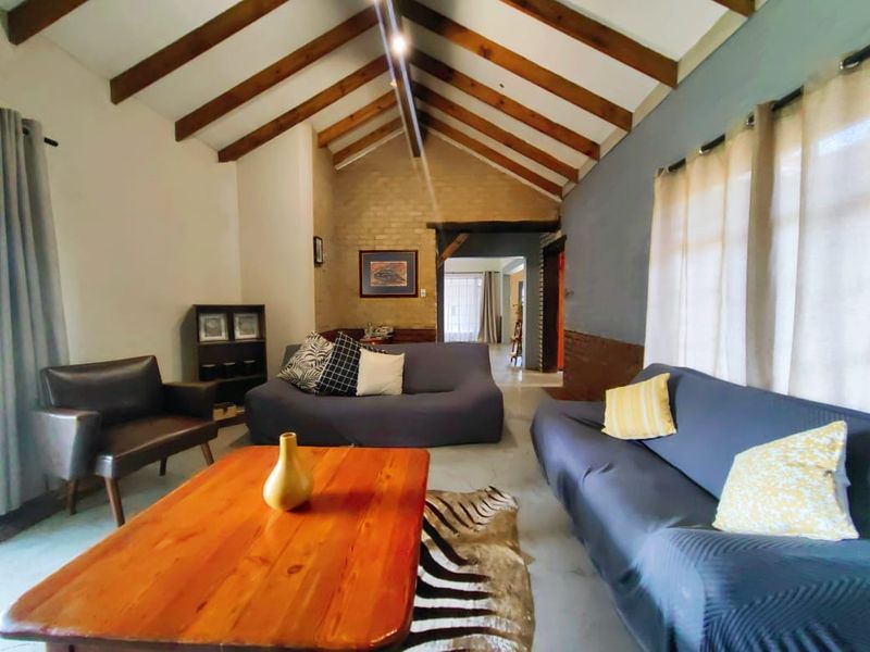 Spacious living room featuring a vaulted ceiling with exposed timber beams, polished concrete floors, and an attractive exposed brick feature wall.
