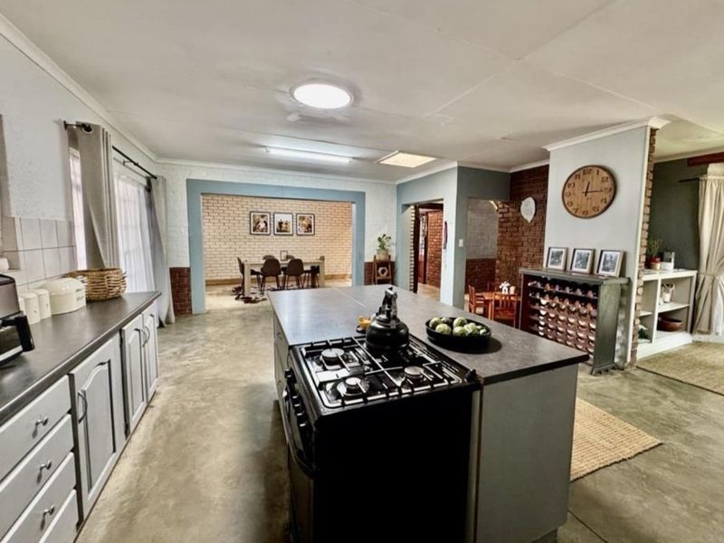 Spacious open-plan kitchen featuring a central island with a gas hob, polished concrete floors, and exposed brick accents, flowing into the dining area.