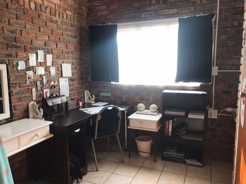A home office space featuring exposed brick walls, tiled flooring, and a window, providing a rustic aesthetic suitable for a workspace.