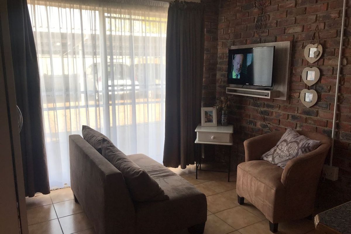 A cozy living room featuring an exposed brick feature wall, ceramic floor tiles, and a sliding glass door providing natural light.