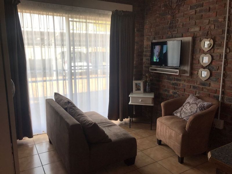 A cozy living room featuring an exposed brick feature wall, ceramic floor tiles, and a sliding glass door providing natural light.