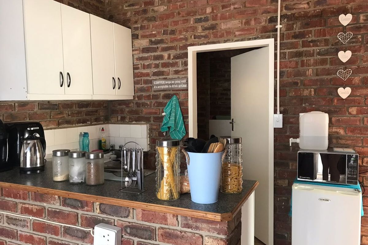 A rustic kitchen area featuring exposed brick walls, white upper cabinetry, and a laminate countertop with a tiled backsplash.