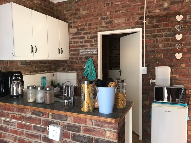 A rustic kitchen area featuring exposed brick walls, white upper cabinetry, and a laminate countertop with a tiled backsplash.