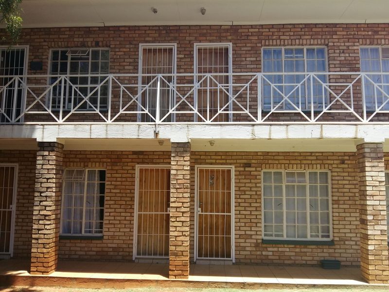 Two-story face brick exterior featuring a ground floor patio and an upper-level balcony with metal security gates and window frames.