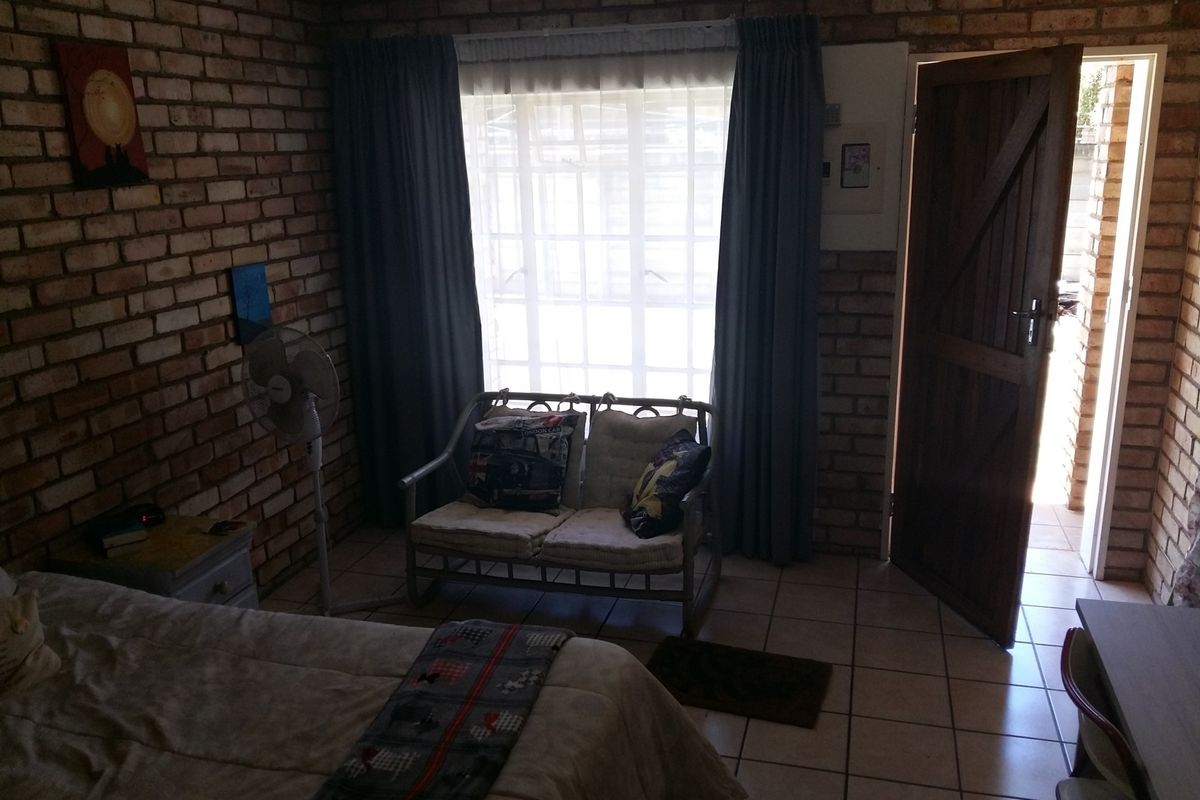 A bedroom featuring exposed brick walls, tiled flooring, and direct access to an outdoor area through a timber door.