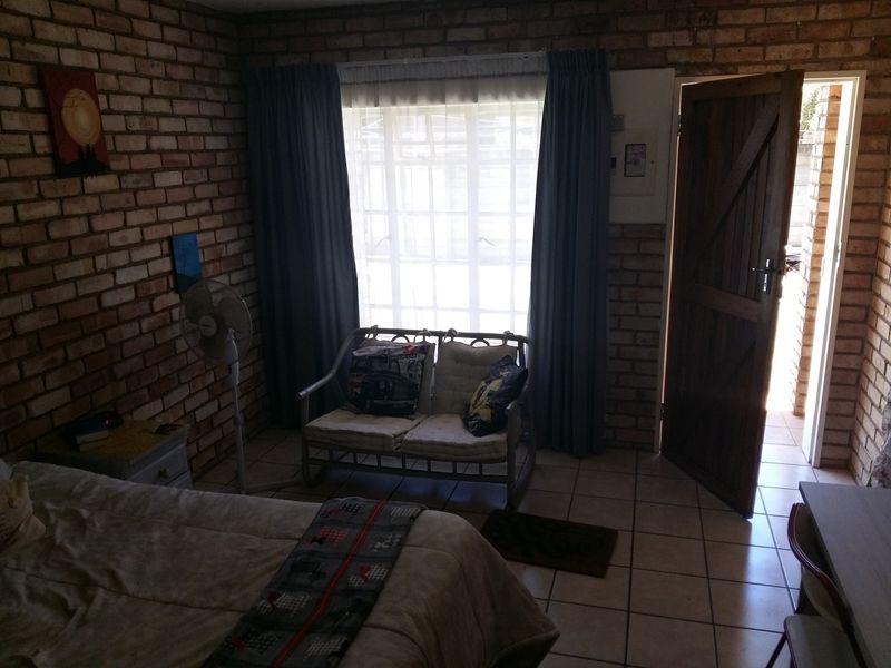 A bedroom featuring exposed brick walls, tiled flooring, and direct access to an outdoor area through a timber door.