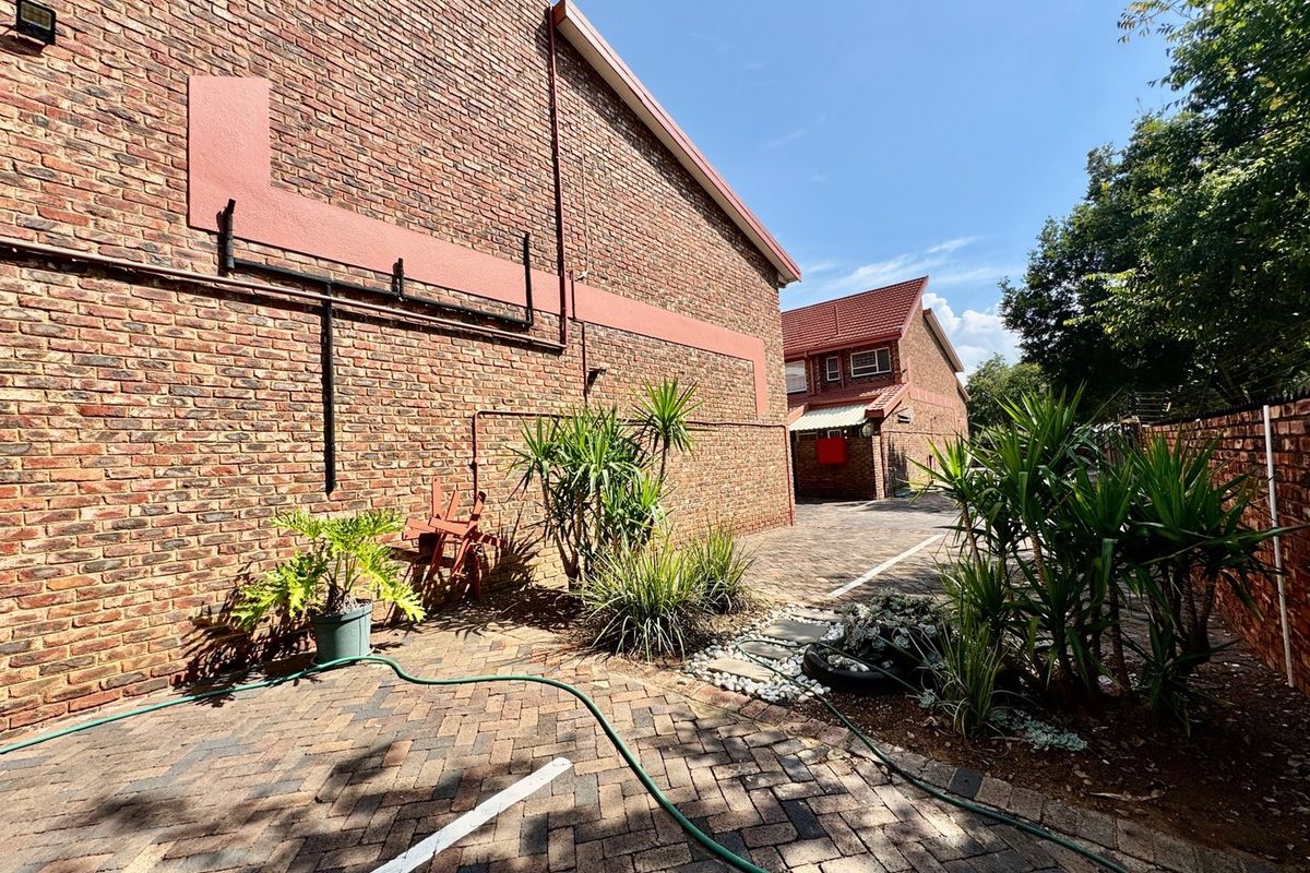 A view of the rear exterior of the townhouse, featuring face brick walls, paved driveway area, and established garden beds.