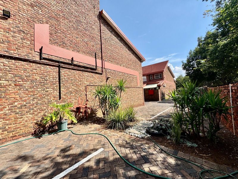 A view of the rear exterior of the townhouse, featuring face brick walls, paved driveway area, and established garden beds.