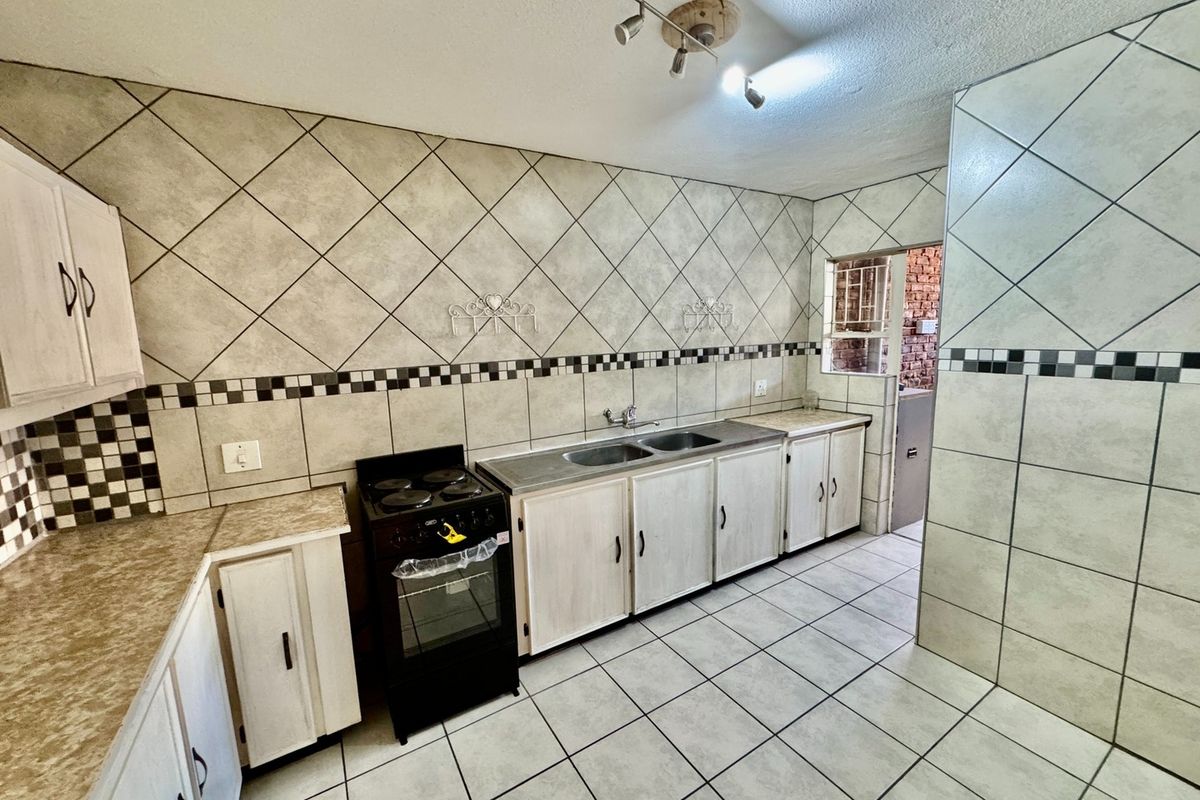 A functional kitchen featuring tiled walls and flooring, built-in cabinetry, a double basin sink, and a freestanding stove.