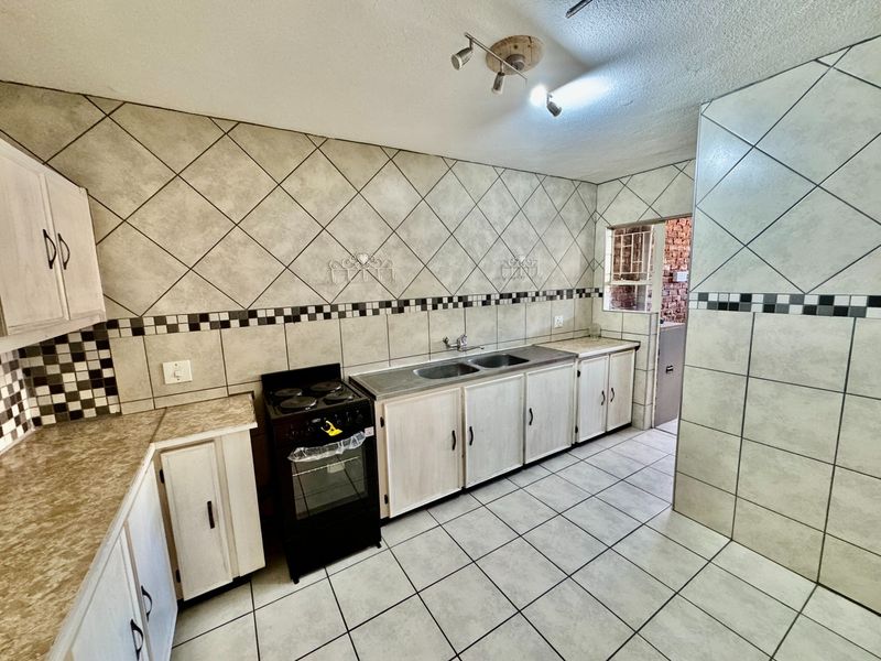 A functional kitchen featuring tiled walls and flooring, built-in cabinetry, a double basin sink, and a freestanding stove.
