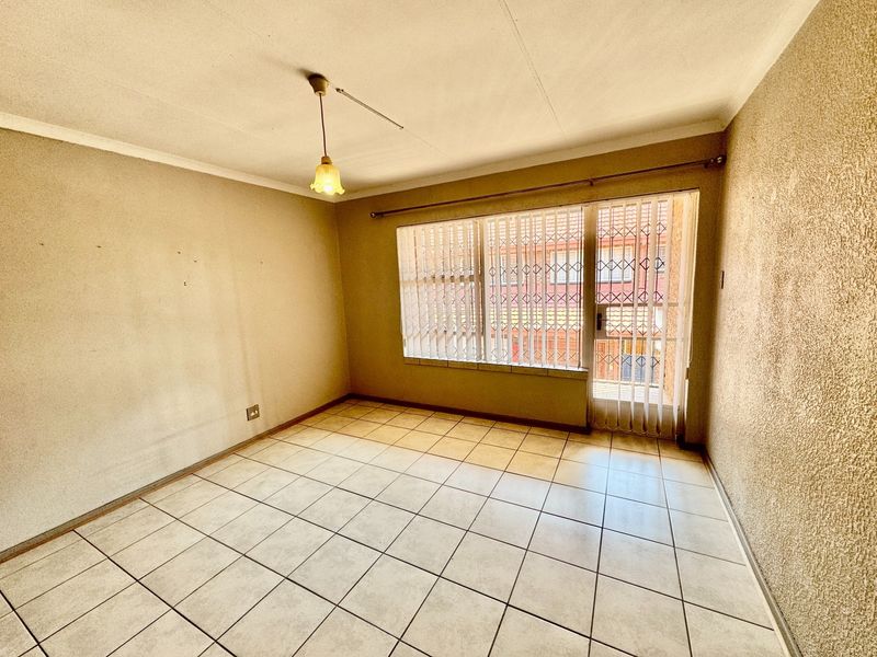 An empty living room featuring tiled flooring, textured walls, and a security gate leading to an outdoor area.
