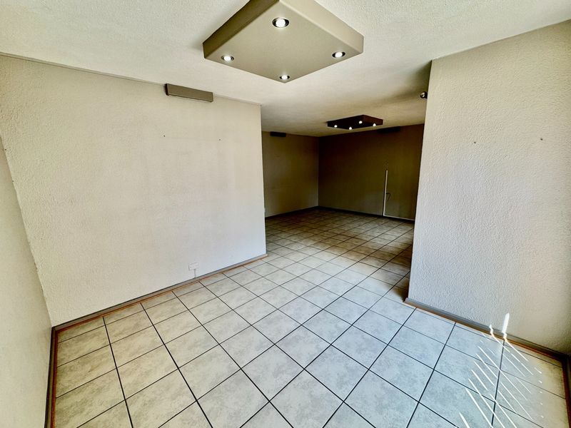 An empty, open-plan living area featuring neutral tiled flooring and modern recessed ceiling lighting, offering a blank canvas for interior design.