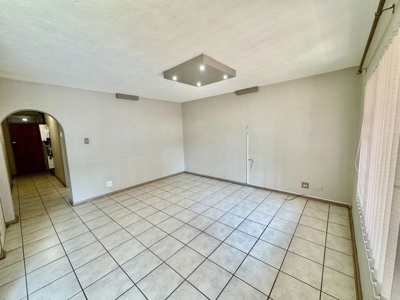An empty living room featuring neutral ceramic floor tiles, an arched entryway, and a modern recessed ceiling light fixture.