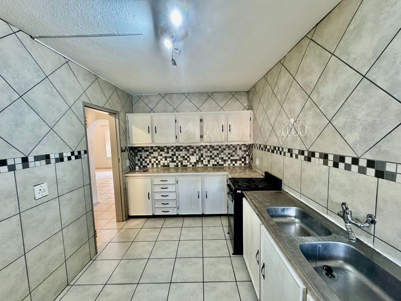 A functional kitchen featuring tiled walls and flooring, built-in cabinetry, a double bowl stainless steel sink, and a freestanding stove.