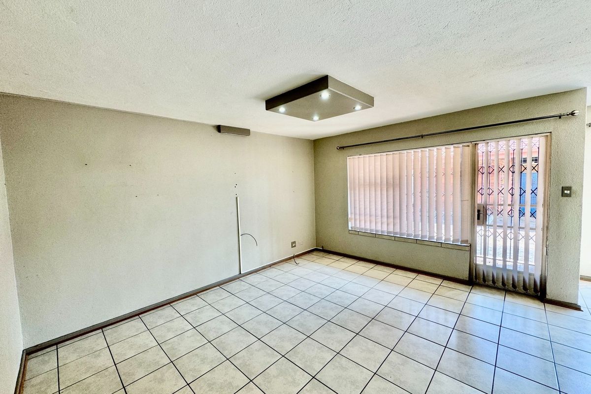 An empty living room featuring tiled flooring, a modern ceiling light fixture, and a sliding glass door with an integrated security gate.