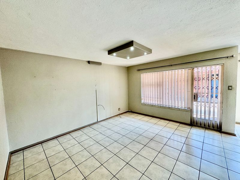 An empty living room featuring tiled flooring, a modern ceiling light fixture, and a sliding glass door with an integrated security gate.