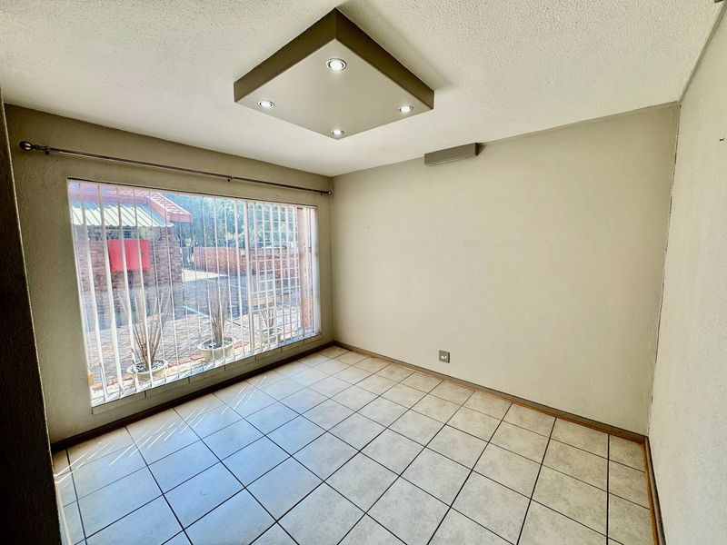 A bright, empty bedroom featuring neutral tiled flooring, a modern recessed ceiling light, and a large window fitted with security bars.
