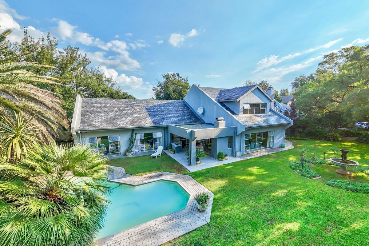 Aerial view of the rear elevation featuring a swimming pool, paved patio area, covered outdoor space, and a well-maintained garden.